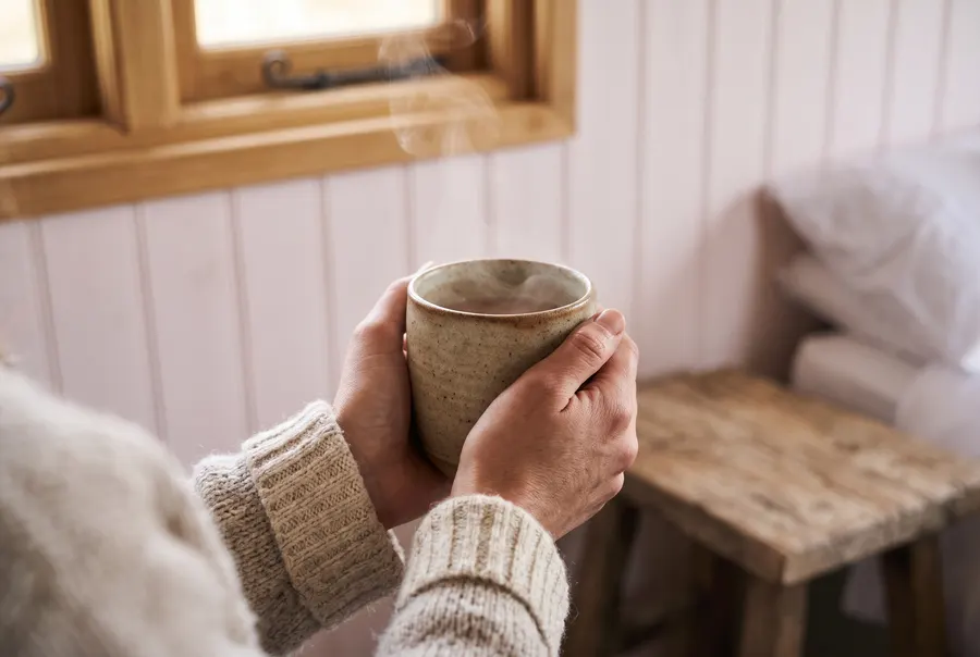 Two hands wrapped around a steaming ceramic mug, in a cosy wood-panelled room